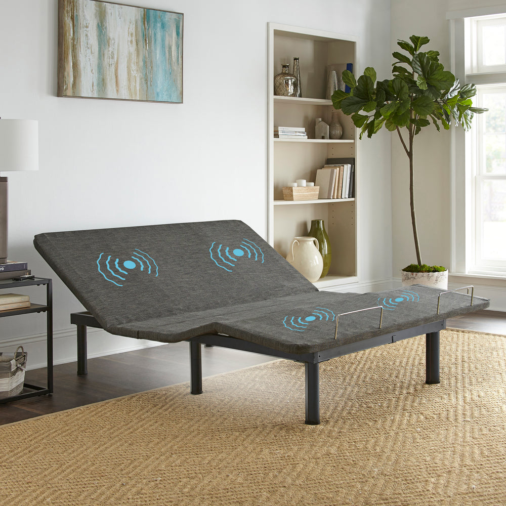 An adjustable power base bed with a gray fabric surface and blue illuminated control buttons, placed in a well-lit living room setting.