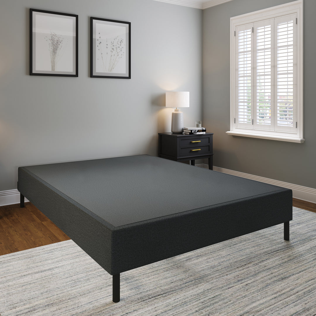 A black platform bed frame with a custom fitted fabric cover, placed in a room with a windowsill decor and a lamp on the nightstand.
