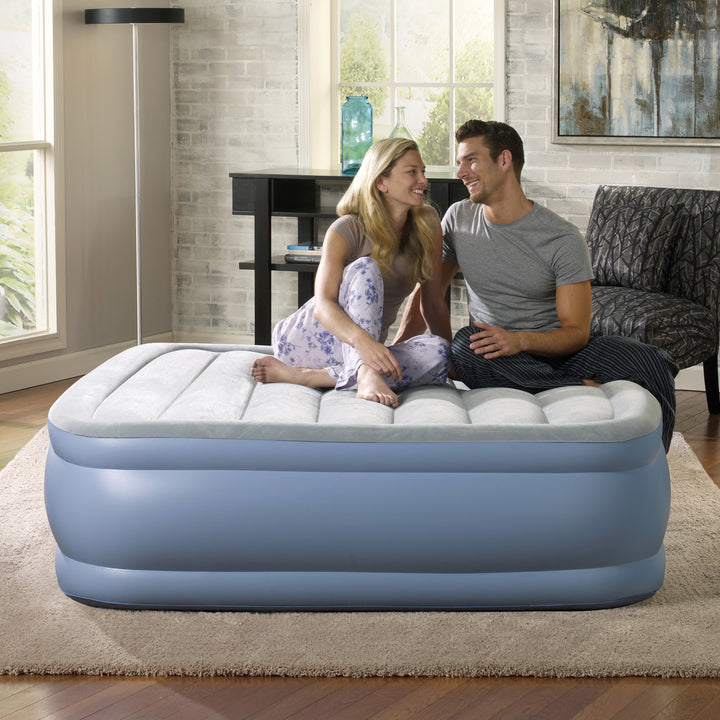 Two people sitting on an inflatable air mattress in a living room.